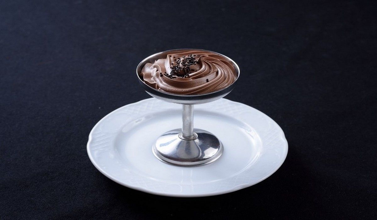 Un tazón de mousse de chocolate en un plato blanco con una cuchara.