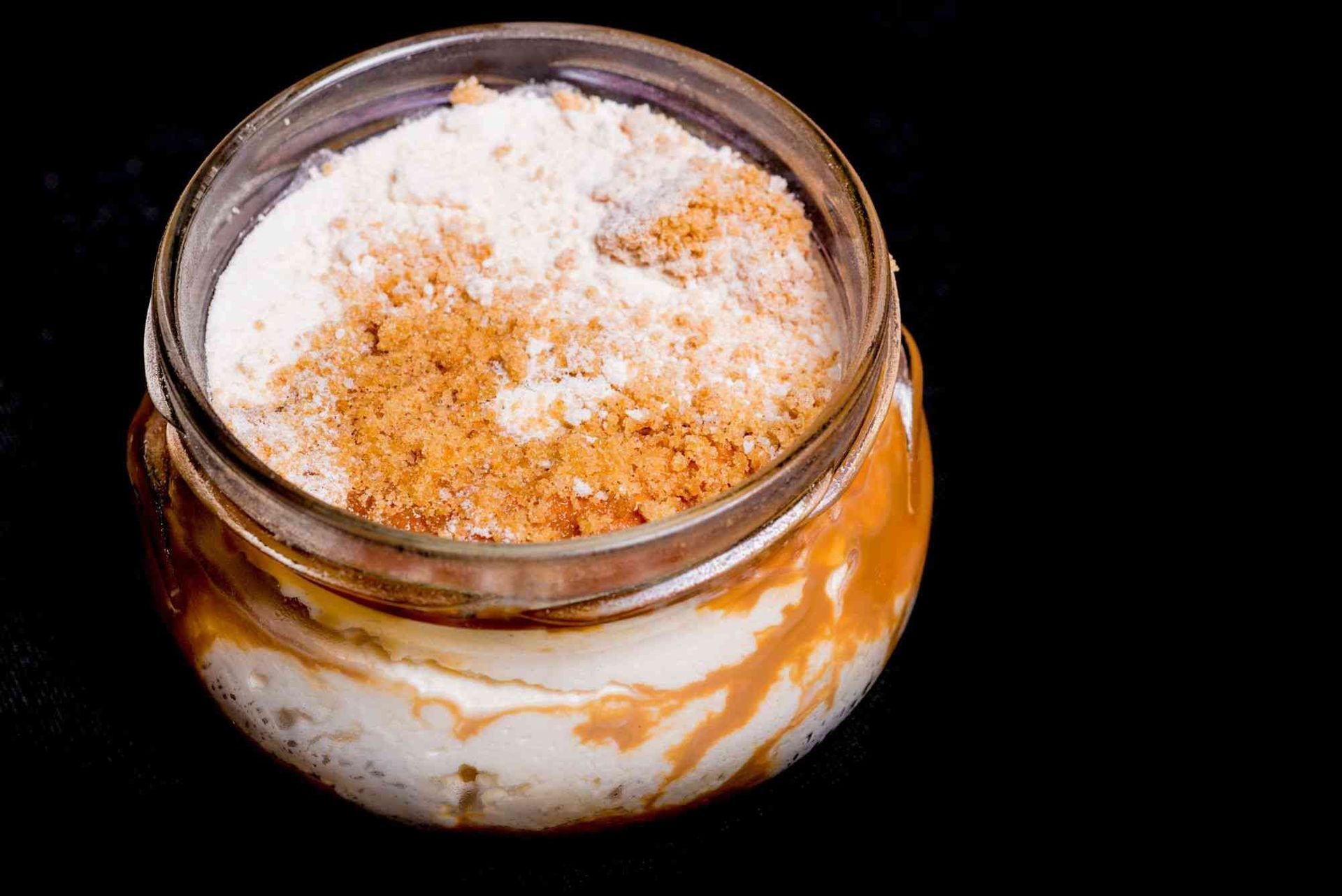 Un frasco lleno de un postre con azúcar en polvo encima.