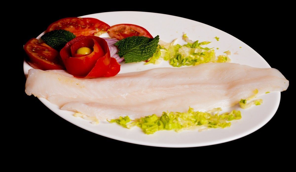 Un plato blanco cubierto con carne y verduras sobre un fondo negro.