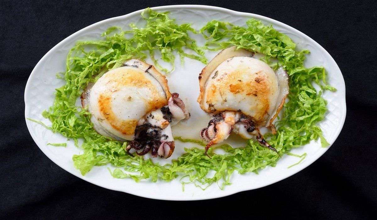 Un plato blanco cubierto con calamares y lechuga sobre un fondo negro.