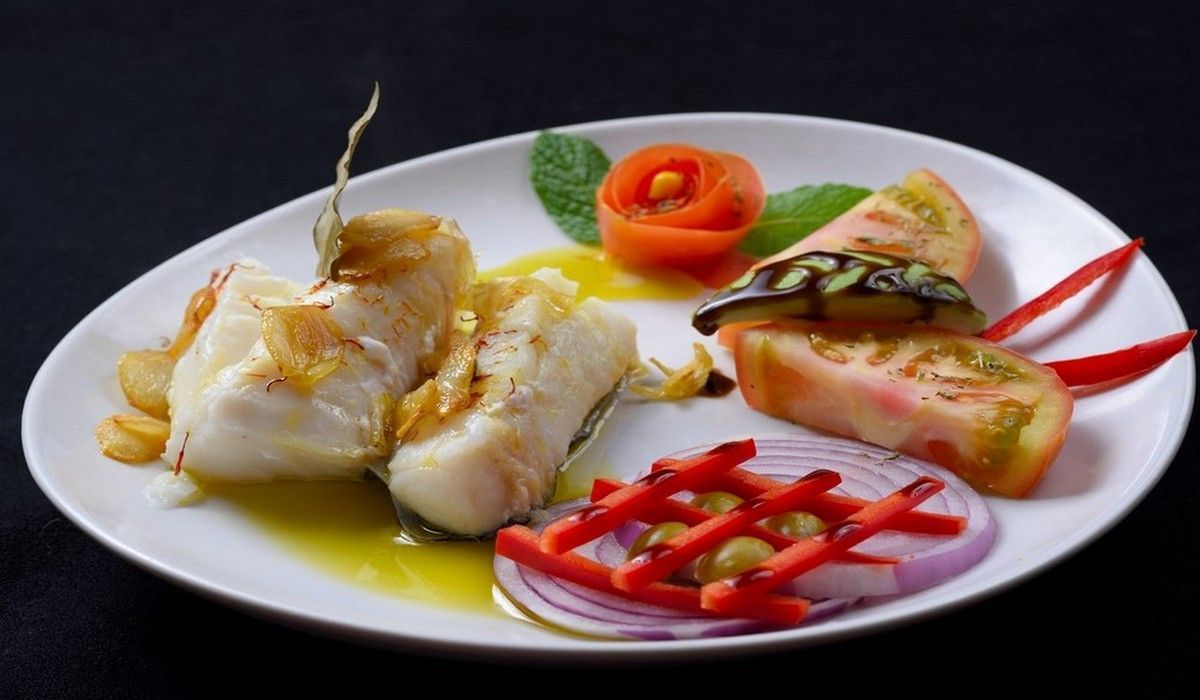 Un plato blanco cubierto con pescado y verduras sobre una mesa.