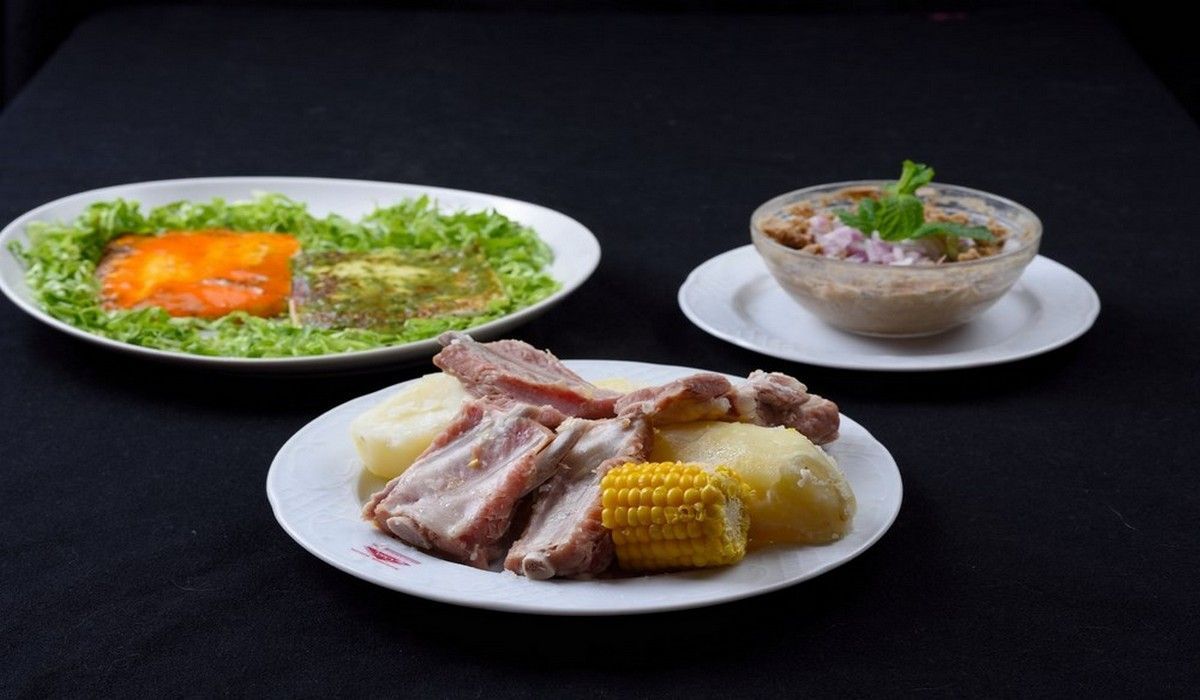 Tres platos de comida en una mesa que incluyen mazorcas de maíz y carne.