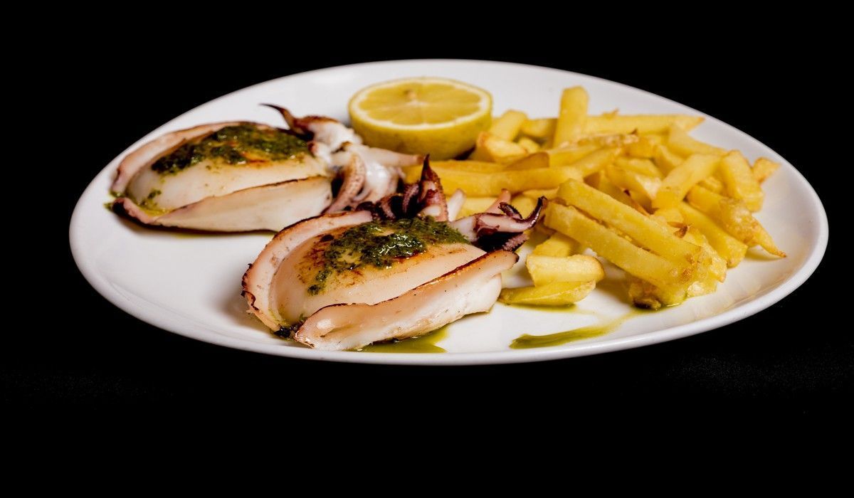 Un plato blanco cubierto con calamares y patatas fritas sobre un fondo negro.
