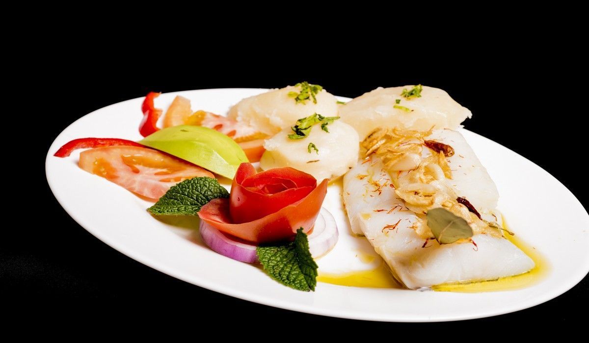 Un plato blanco cubierto con pescado y verduras sobre un fondo negro.