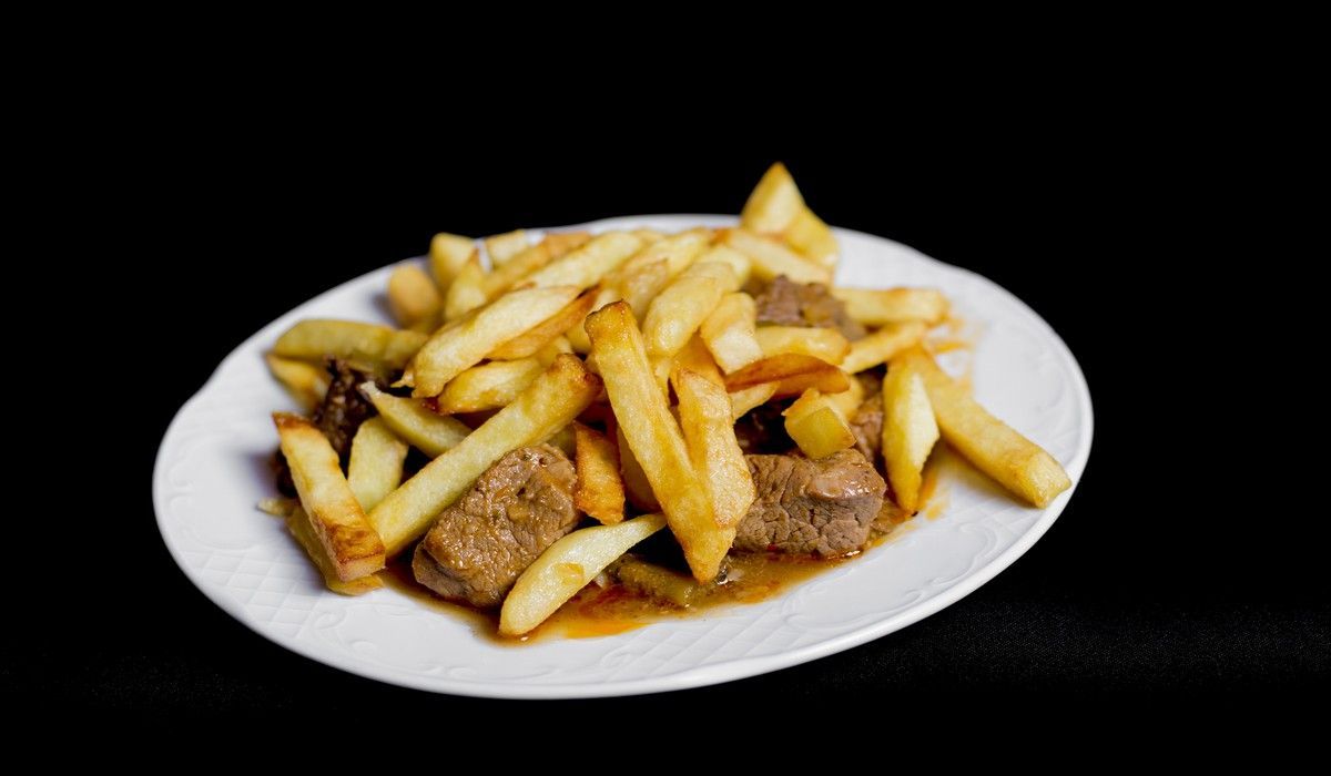 Un plato blanco cubierto con papas fritas y carne sobre un fondo negro.