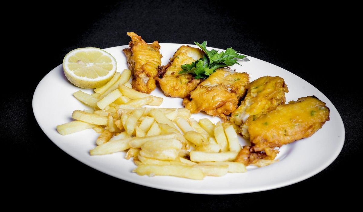 Un plato blanco cubierto con pescado frito y papas fritas.