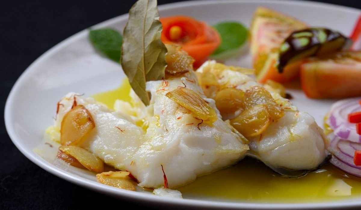 Un plato blanco cubierto con pescado y verduras sobre una mesa.
