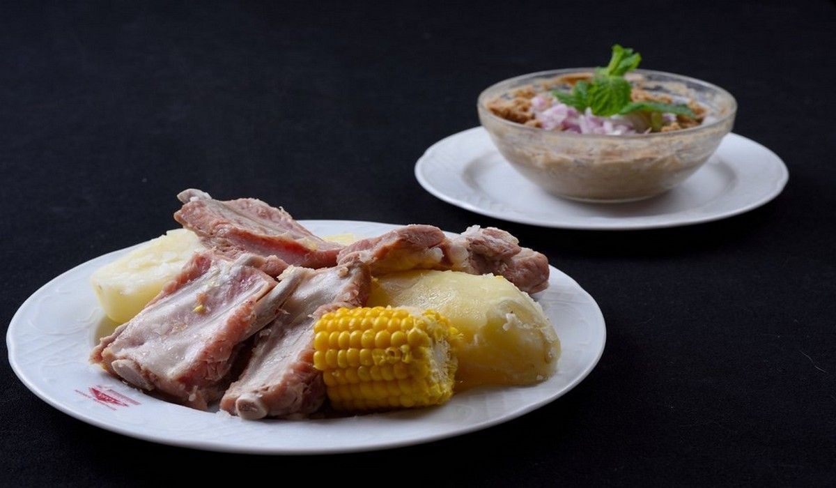 Un plato de comida con maíz y patatas junto a un tazón de sopa.