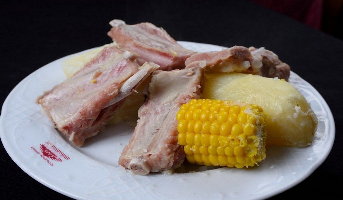 Un plato blanco cubierto con carne, patatas y mazorcas de maíz.