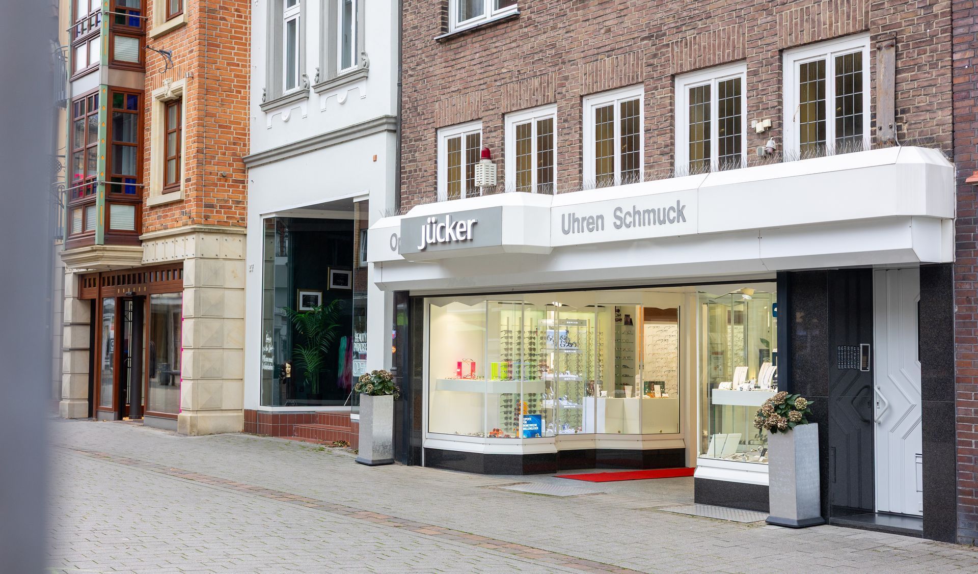 Straßenansicht eines weißen Ladengeschäfts mit großen Fenstern in einer mit Ziegelsteinen gepflasterten Fußgängerzone