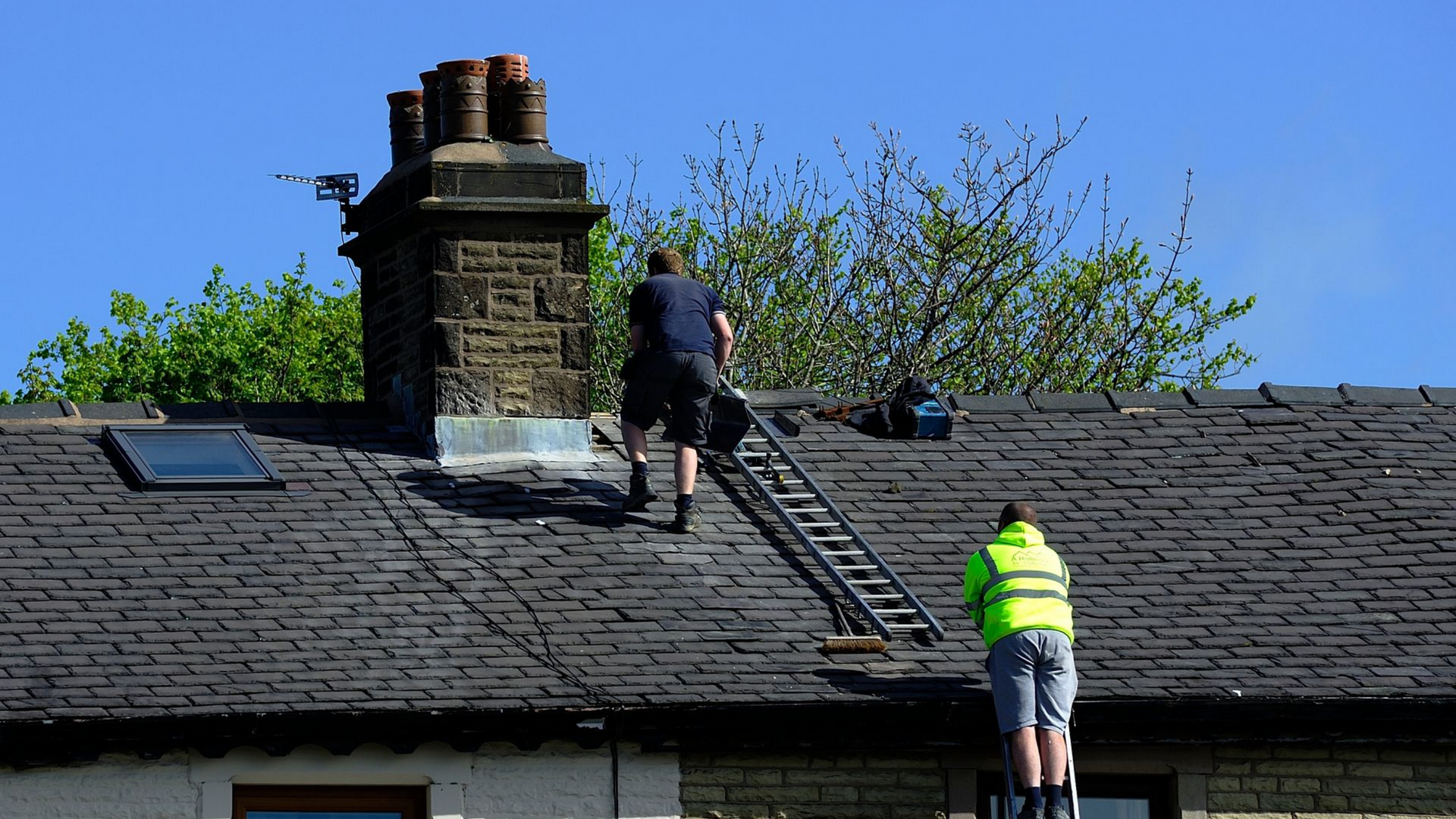 Deux ouvriers installent des panneaux solaires sur un toit de tuiles sous un ciel bleu.