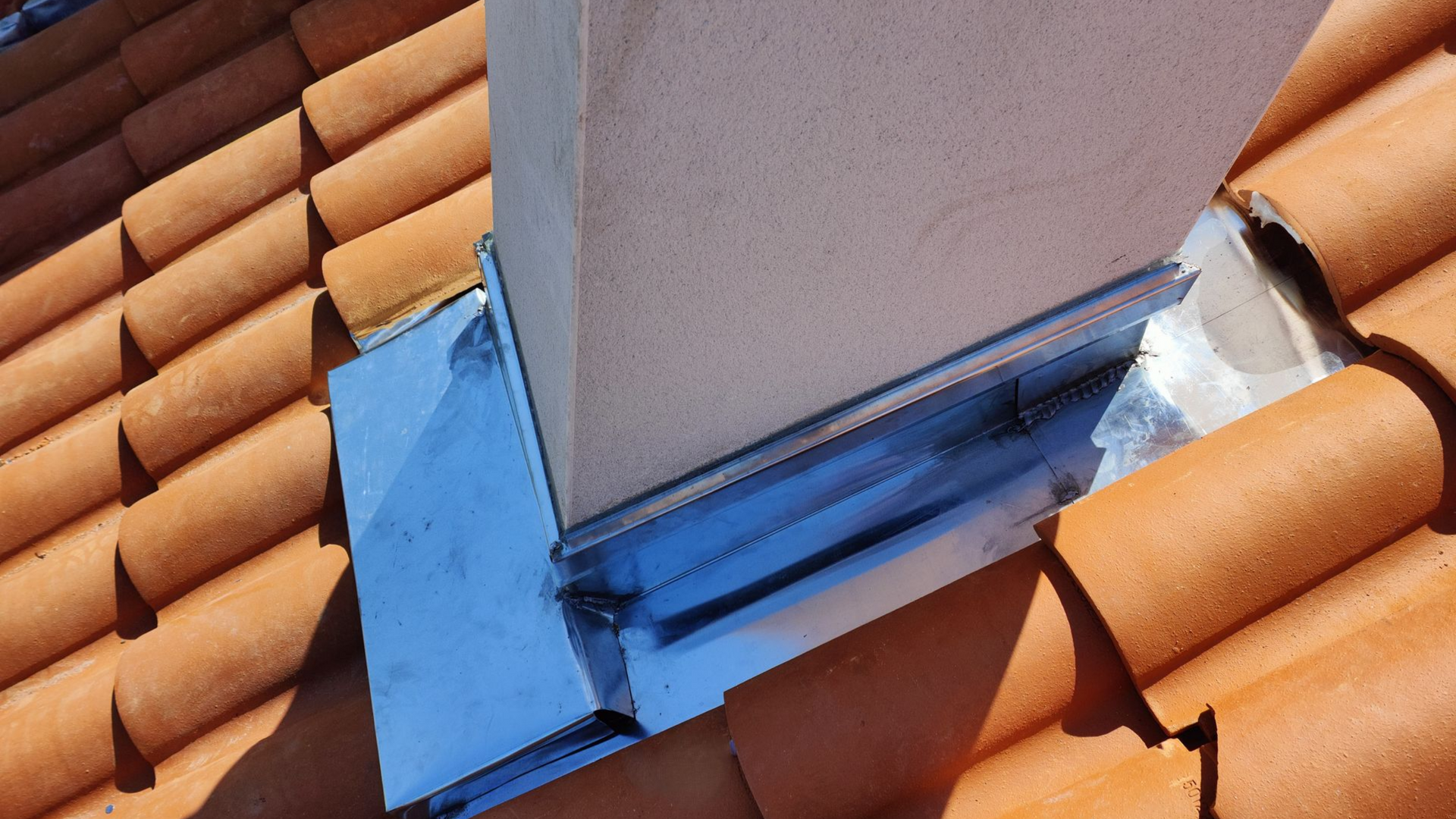 Cheminée sur un toit de tuiles avec solin, inclinée pour l'écoulement des eaux.