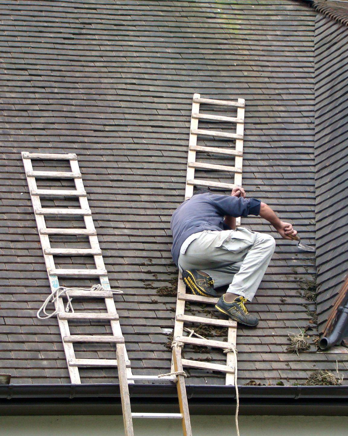Une personne nettoie à haute pression un toit de tuiles rouges, en enlevant les algues et en pulvérisant de l'eau.