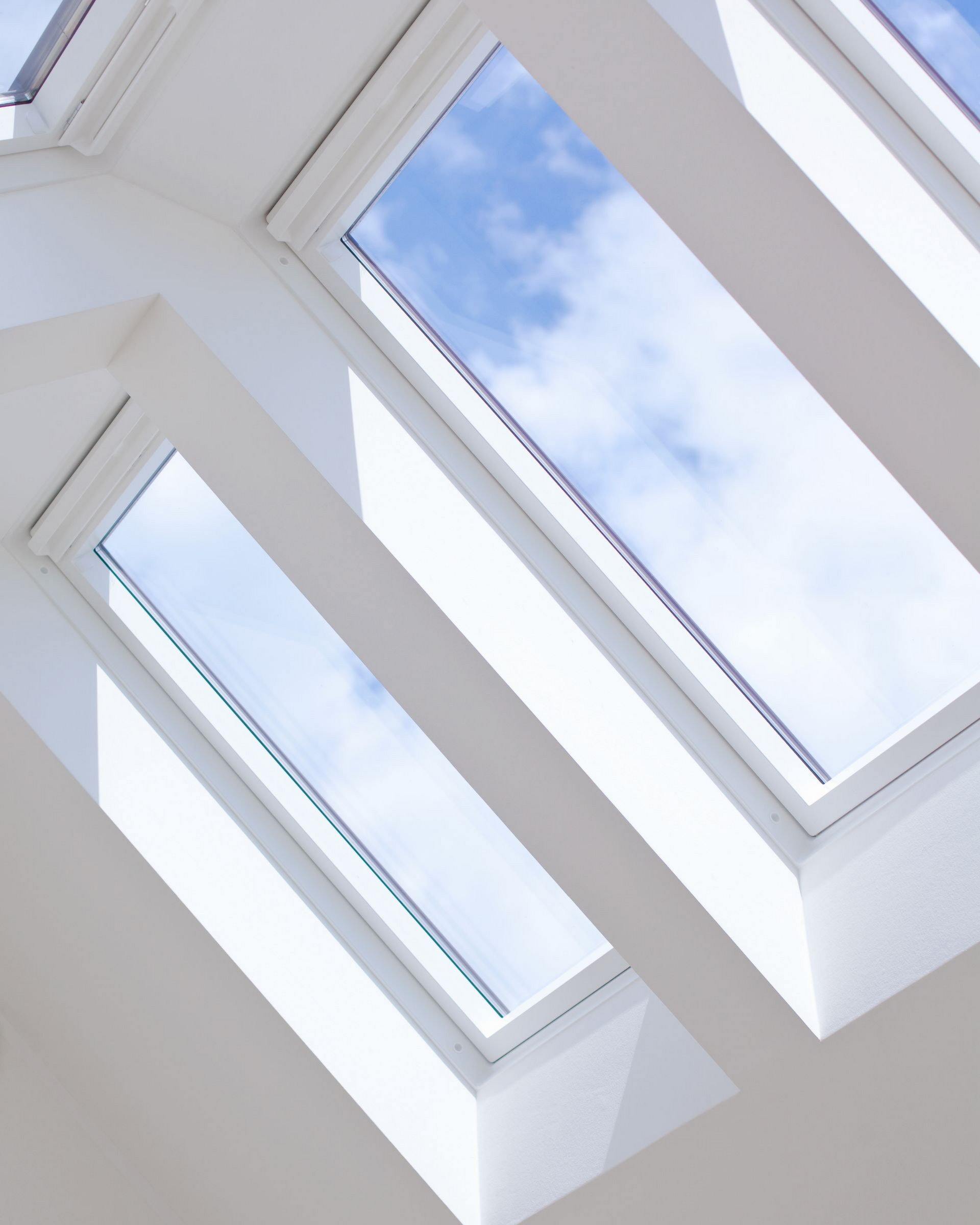 Puits de lumière dans le plafond blanc, offrant une vue sur le ciel bleu nuageux.