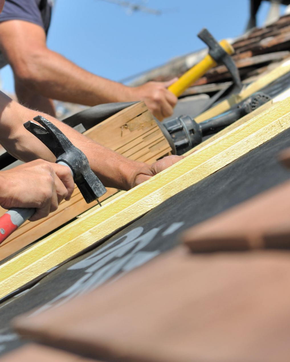 Deux ouvriers posent des tuiles à l'aide de marteaux par une journée ensoleillée.