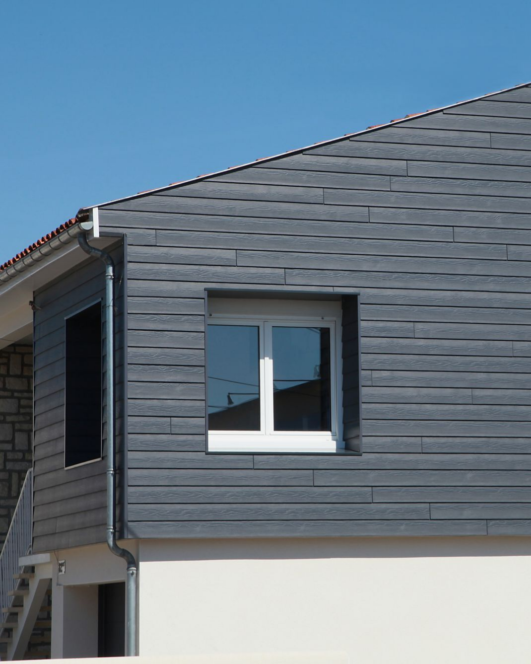 Un bâtiment avec un revêtement gris, une fenêtre blanche et un ciel d'un bleu limpide.