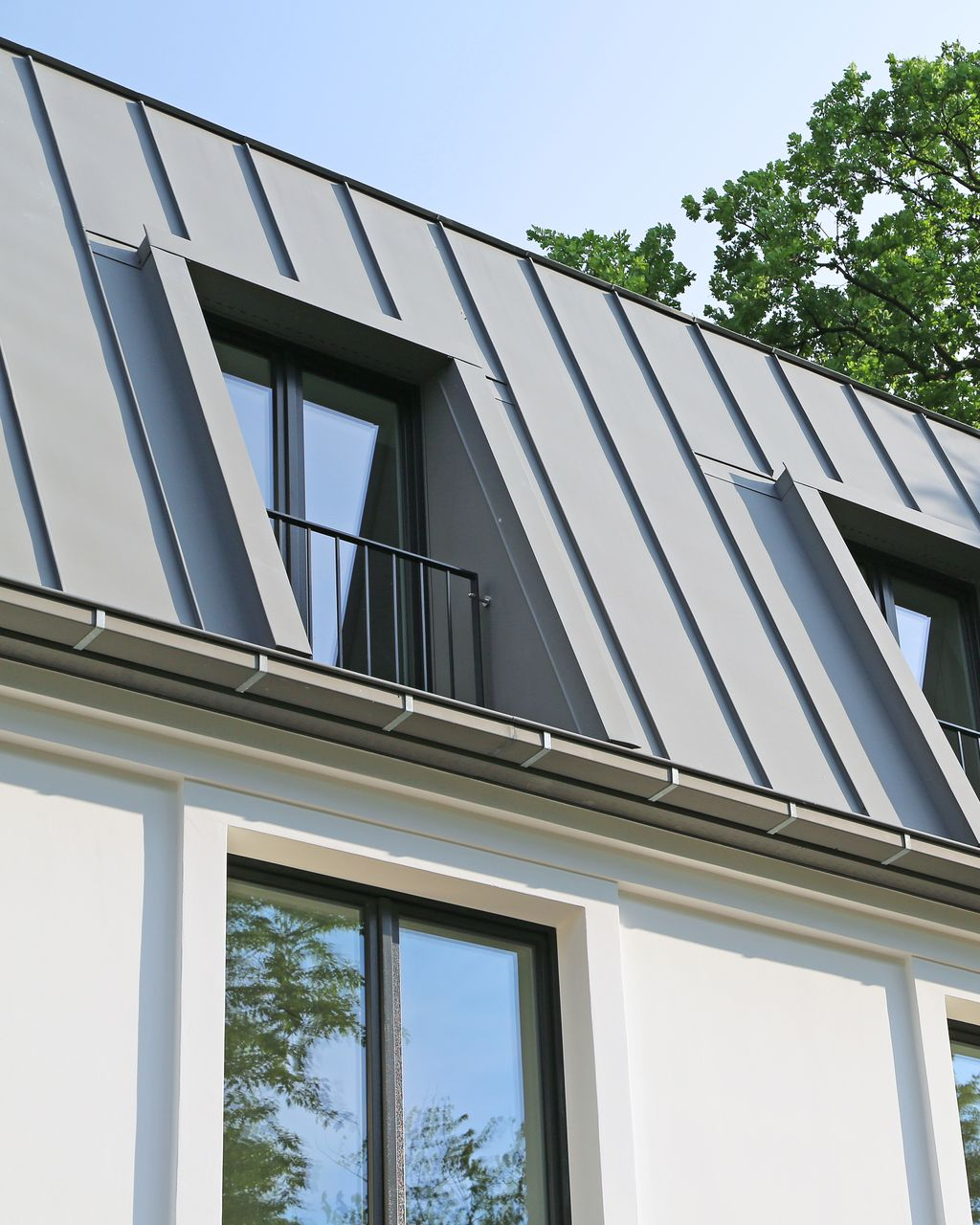 Toiture métallique grise avec lucarnes sur un bâtiment blanc, journée ensoleillée.