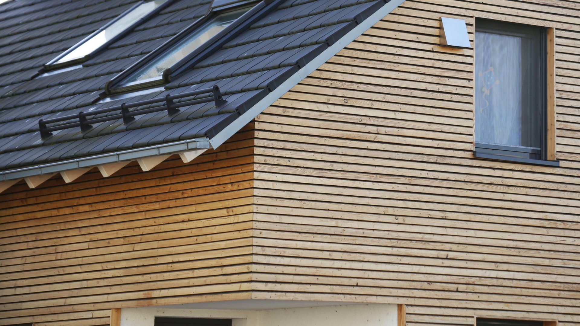 Maison à bardage en bois avec un toit gris foncé, comprenant des puits de lumière et une fenêtre unique.