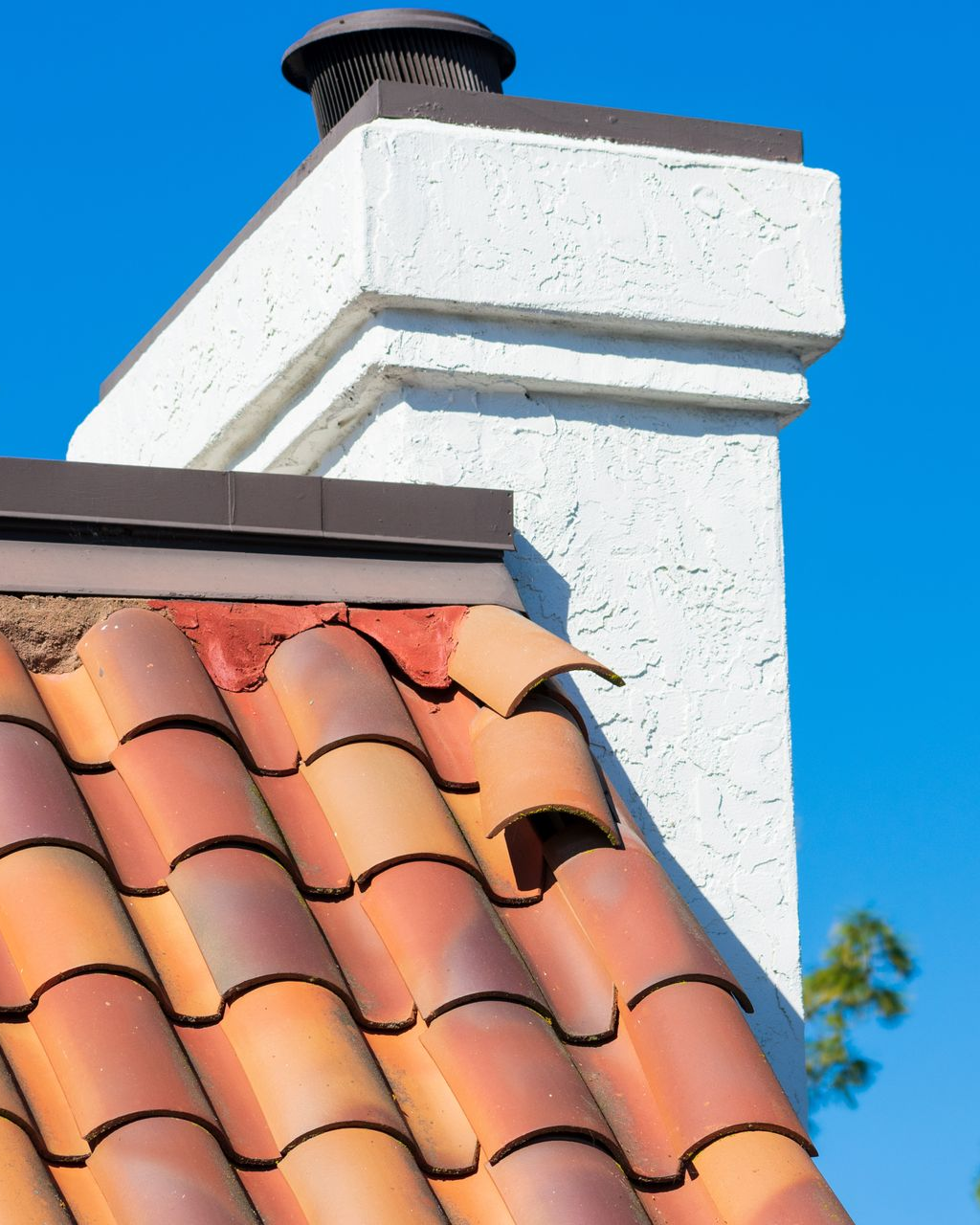 Toit de tuiles en terre cuite et cheminée en stuc sur fond de ciel bleu.