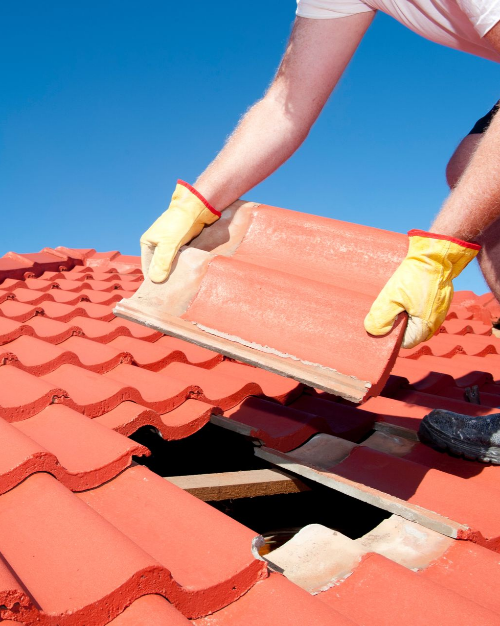 Une personne portant des gants jaunes remplace une tuile rouge par une journée ensoleillée.