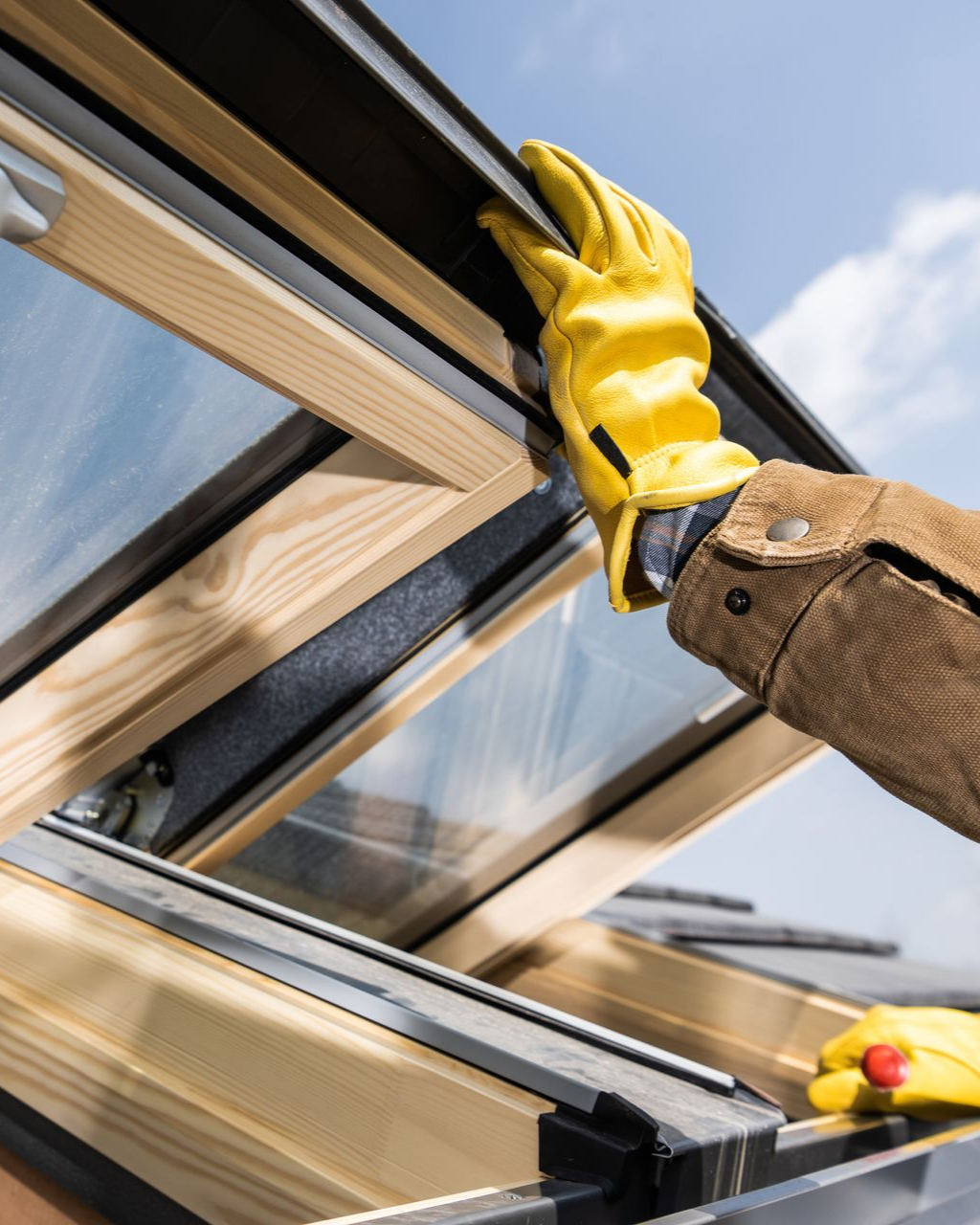 Main gantée de jaune ouvrant une lucarne, ciel bleu en arrière-plan.