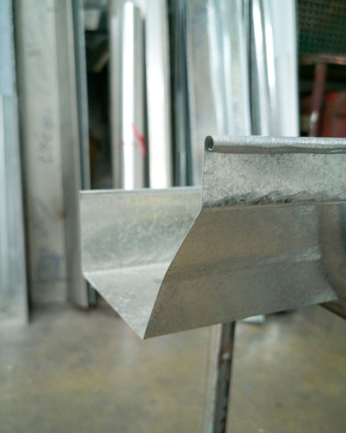 Gouttière métallique, gros plan, coupe en biais, argentée, environnement d'atelier, autres gouttières en arrière-plan.