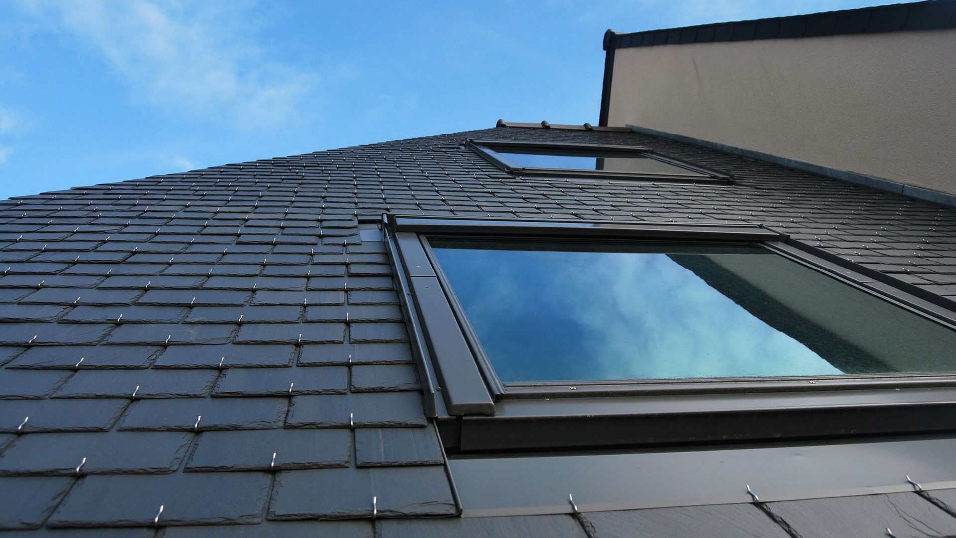 Une lucarne ouverte sur un toit de tuiles grises laisse entrer la lumière naturelle.