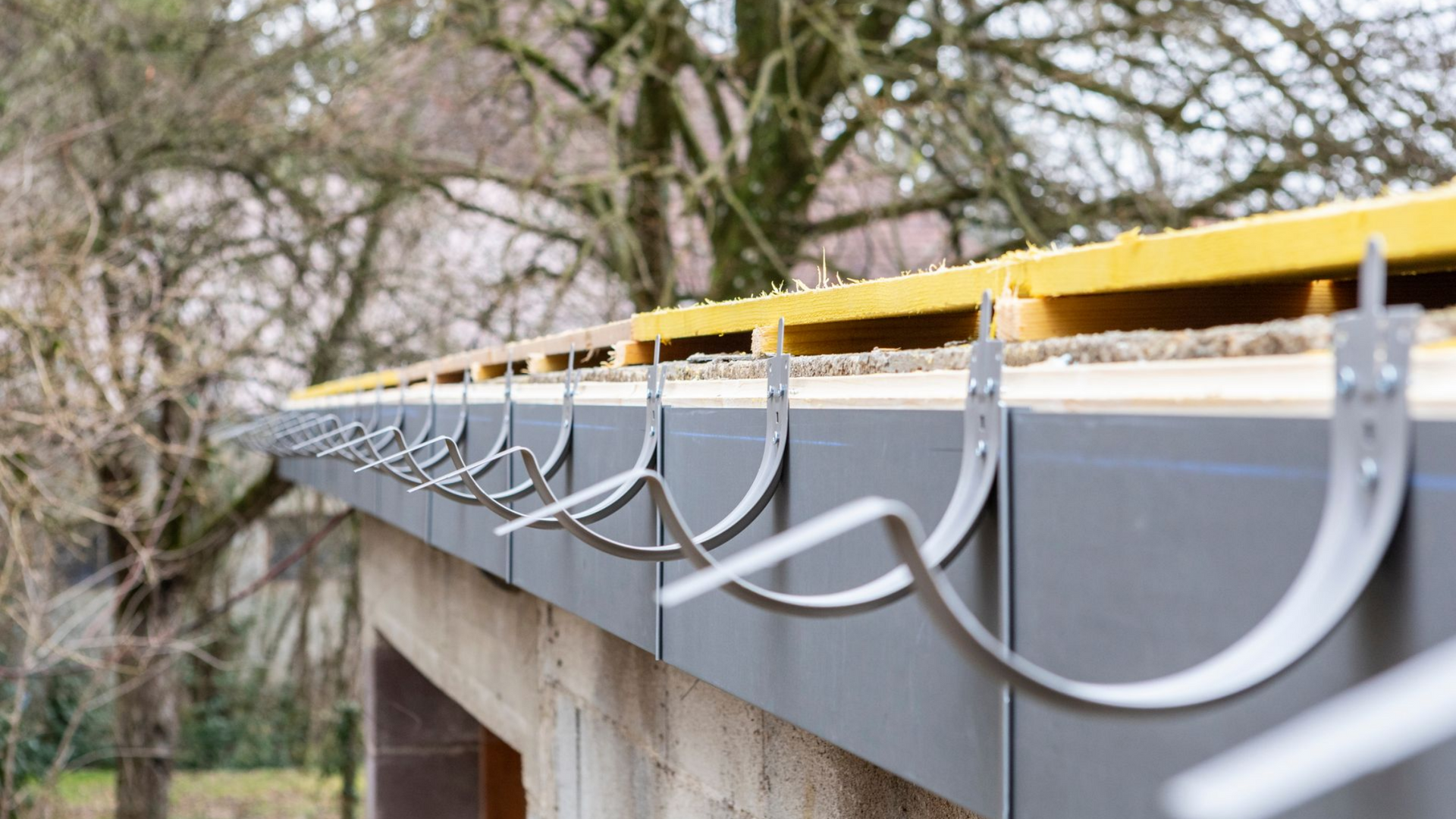 Système de gouttière grise avec supports incurvés fixés au bord du toit d'un bâtiment.