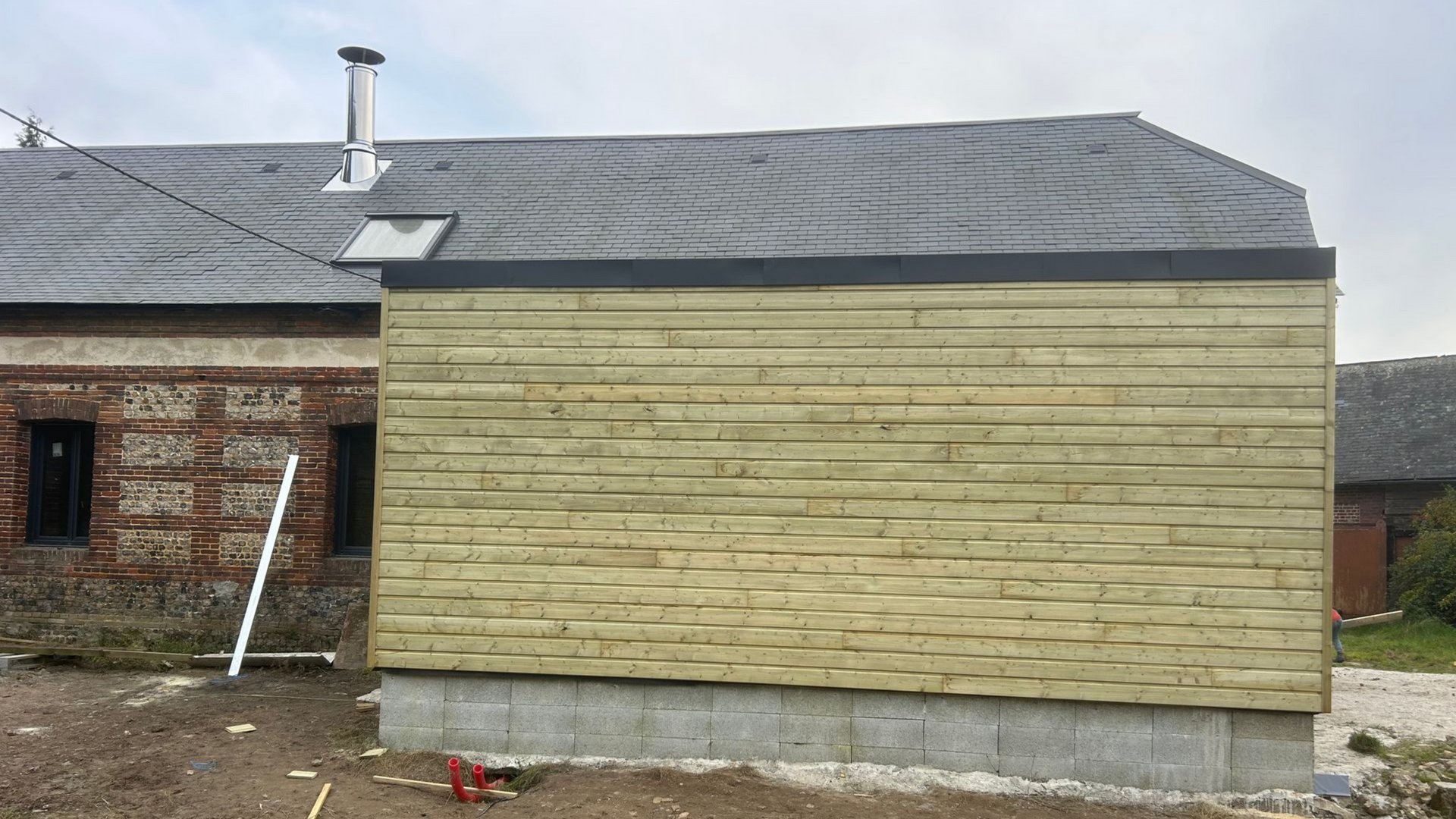 Bâtiment revêtu de bois avec toit sombre, puits de lumière et fenêtres.