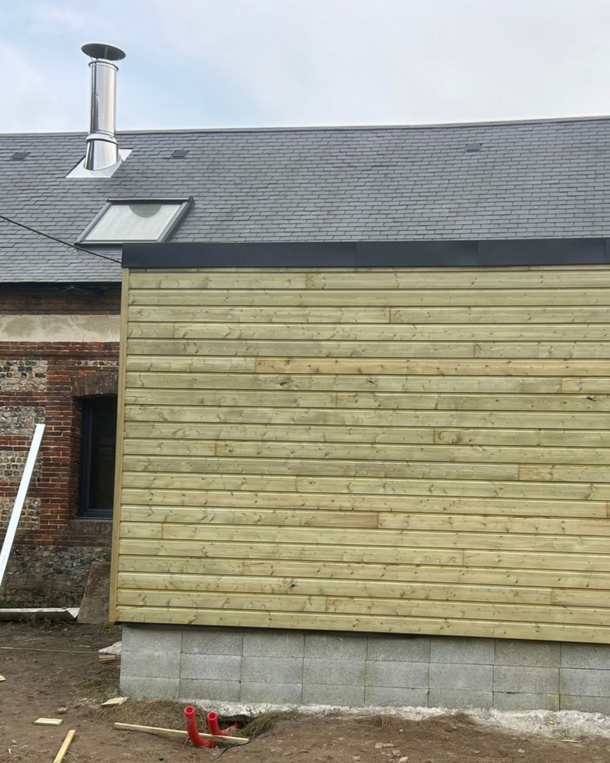 Maison à l'extérieur lambrissé, avec un toit de tuiles foncées, des puits de lumière et une partie inférieure blanche.