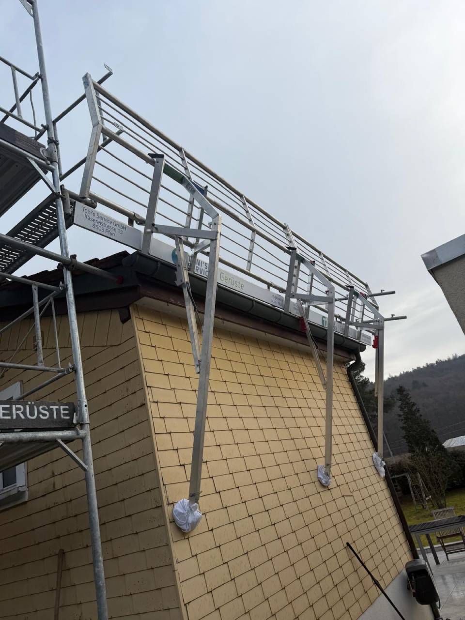 Gebäude wird renoviert, Gerüst mit Plastikfolie abgedeckt. Schild mit grünem Banner, roter Backsteinsockel.