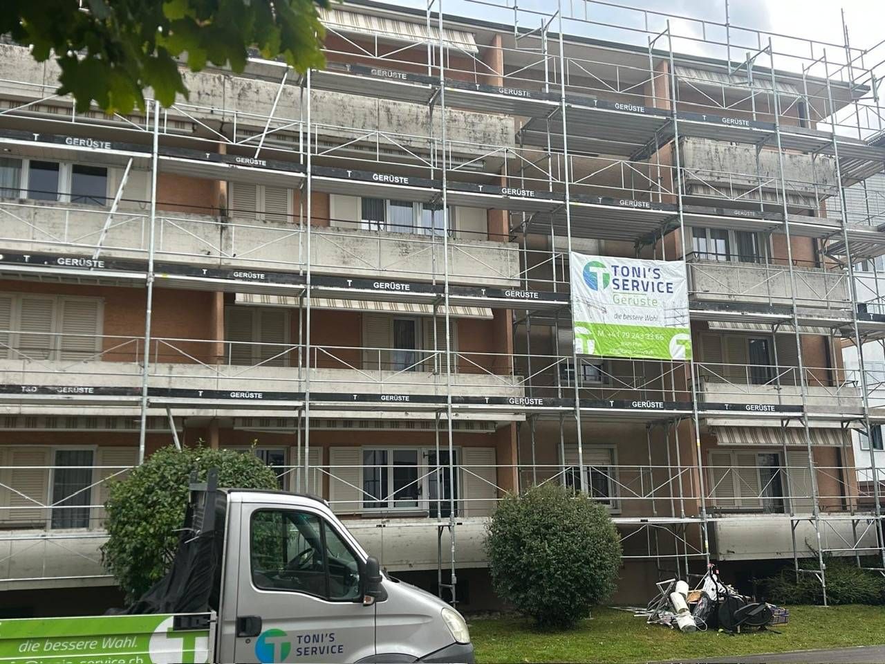 Gebäudefassade wird renoviert und ist eingerüstet; im Vordergrund ein weisser Lieferwagen.