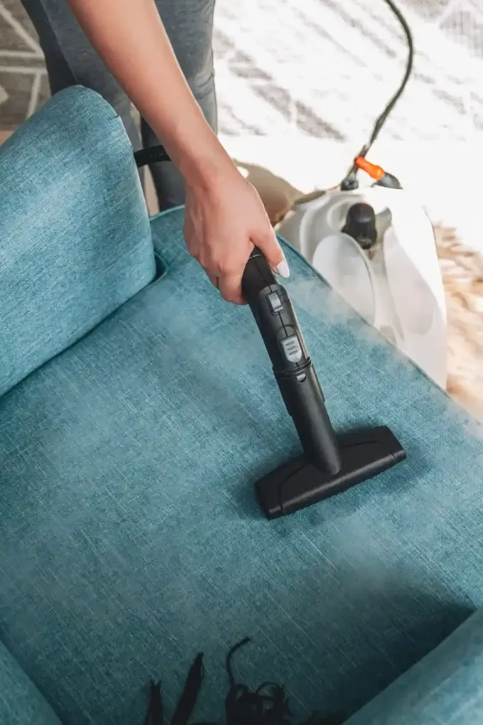 Una persona con guantes azules sostiene un cubo gris que contiene una botella pulverizadora amarilla.