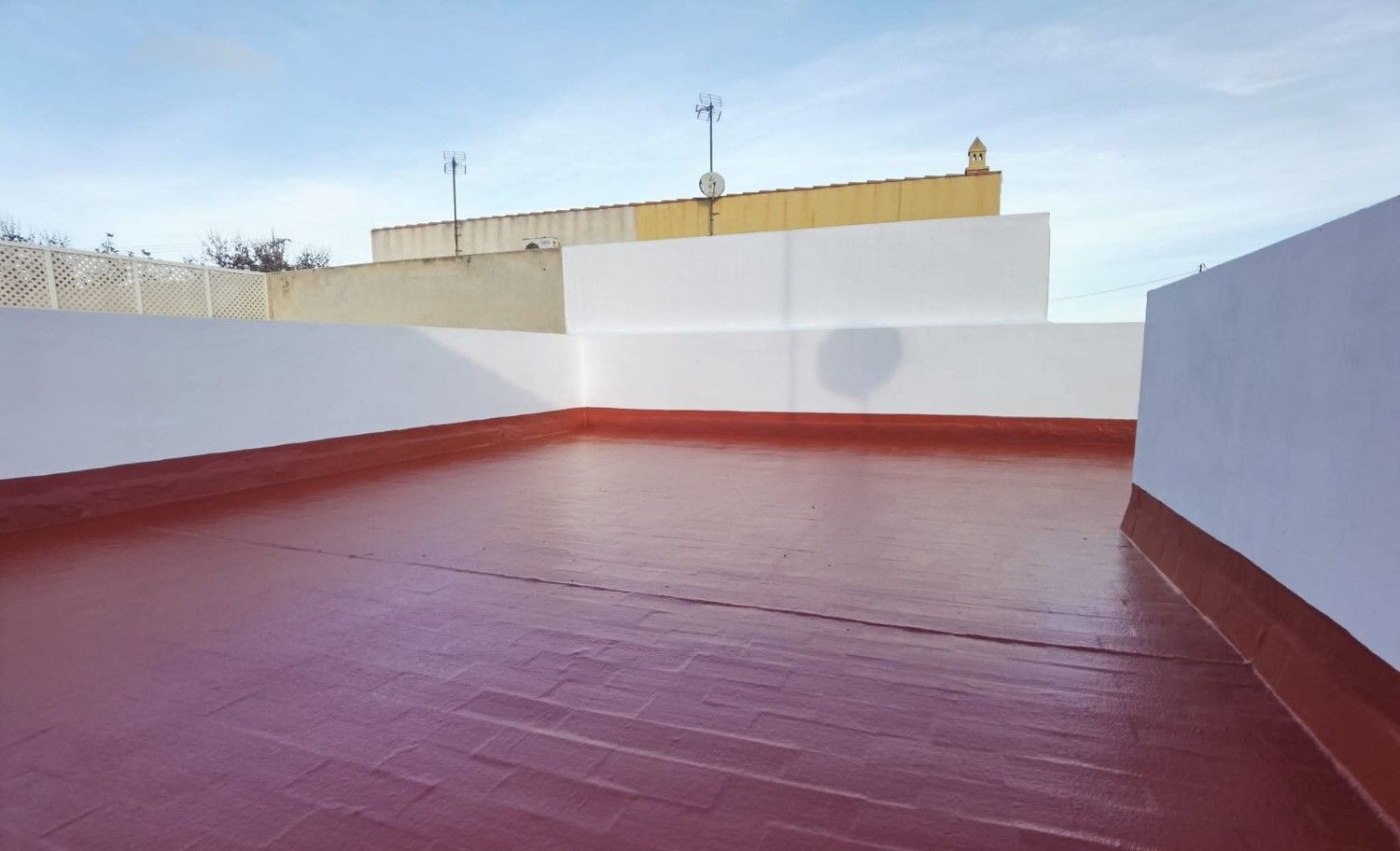 Terraza vacía en la azotea con suelo rojo y paredes blancas bajo un cielo despejado.