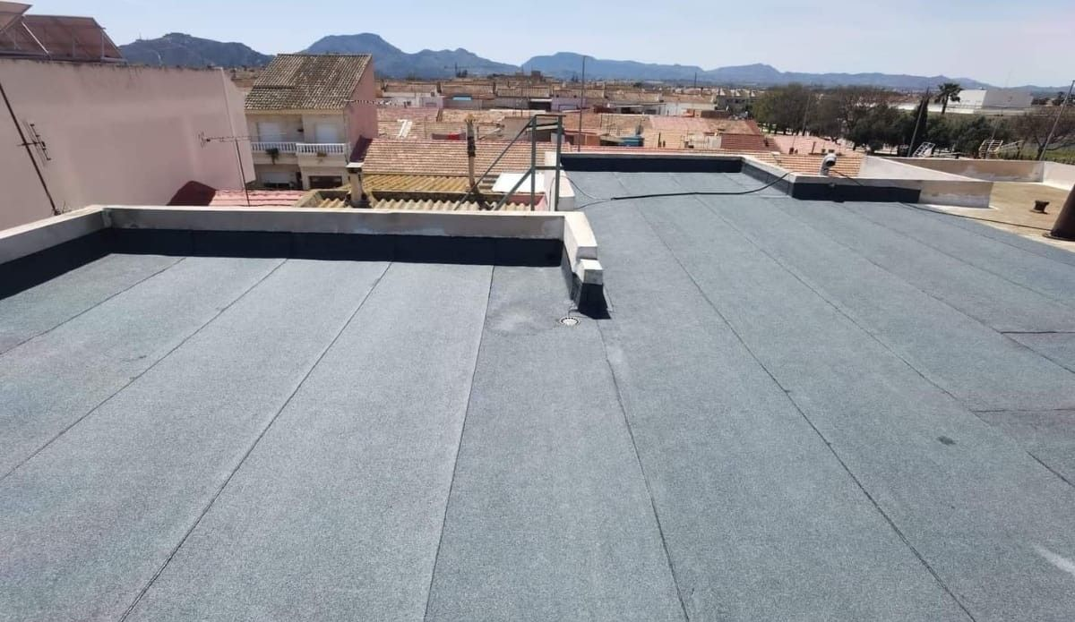 Azotea plana con techo gris con vistas a un pueblo y montañas lejanas bajo un cielo despejado.