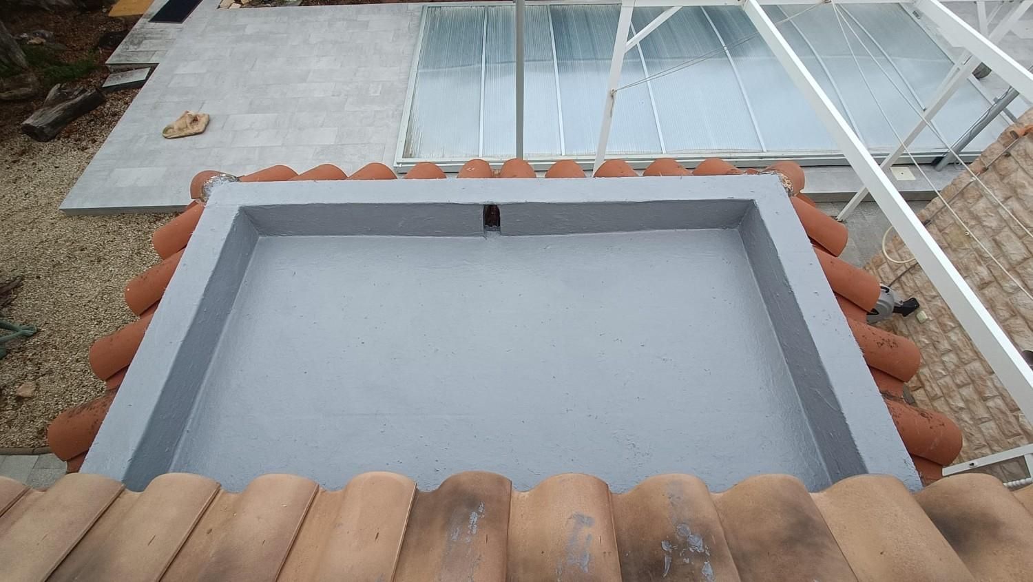 Caja de ventilación gris en la azotea, rodeada de tejas de terracota, en un edificio con techo de cristal.