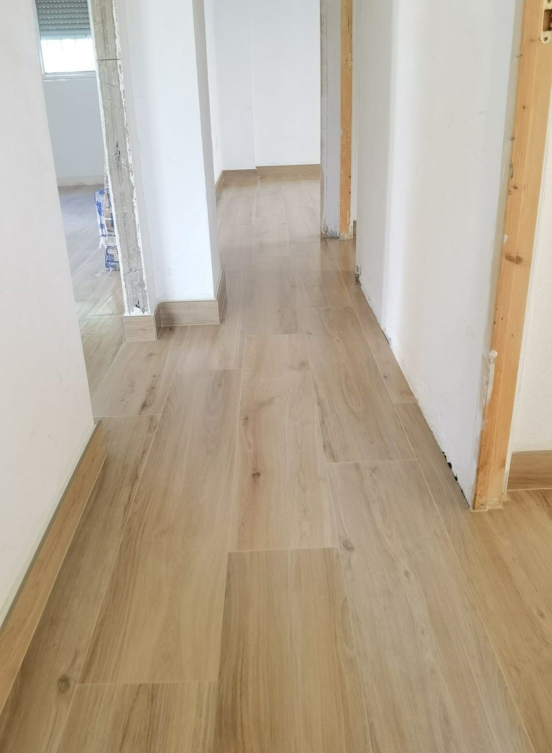 Pasillo estrecho con suelo de madera clara y paredes blancas, con vistas a una puerta y a otra habitación.