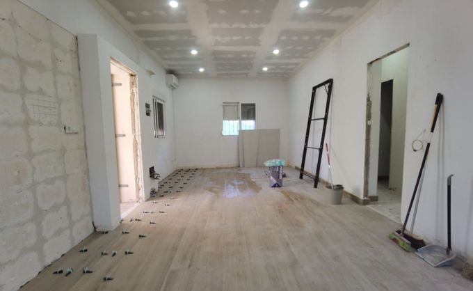 Habitación reformada con paredes blancas, suelo de madera, escaleras y herramientas durante los trabajos de construcción interior.