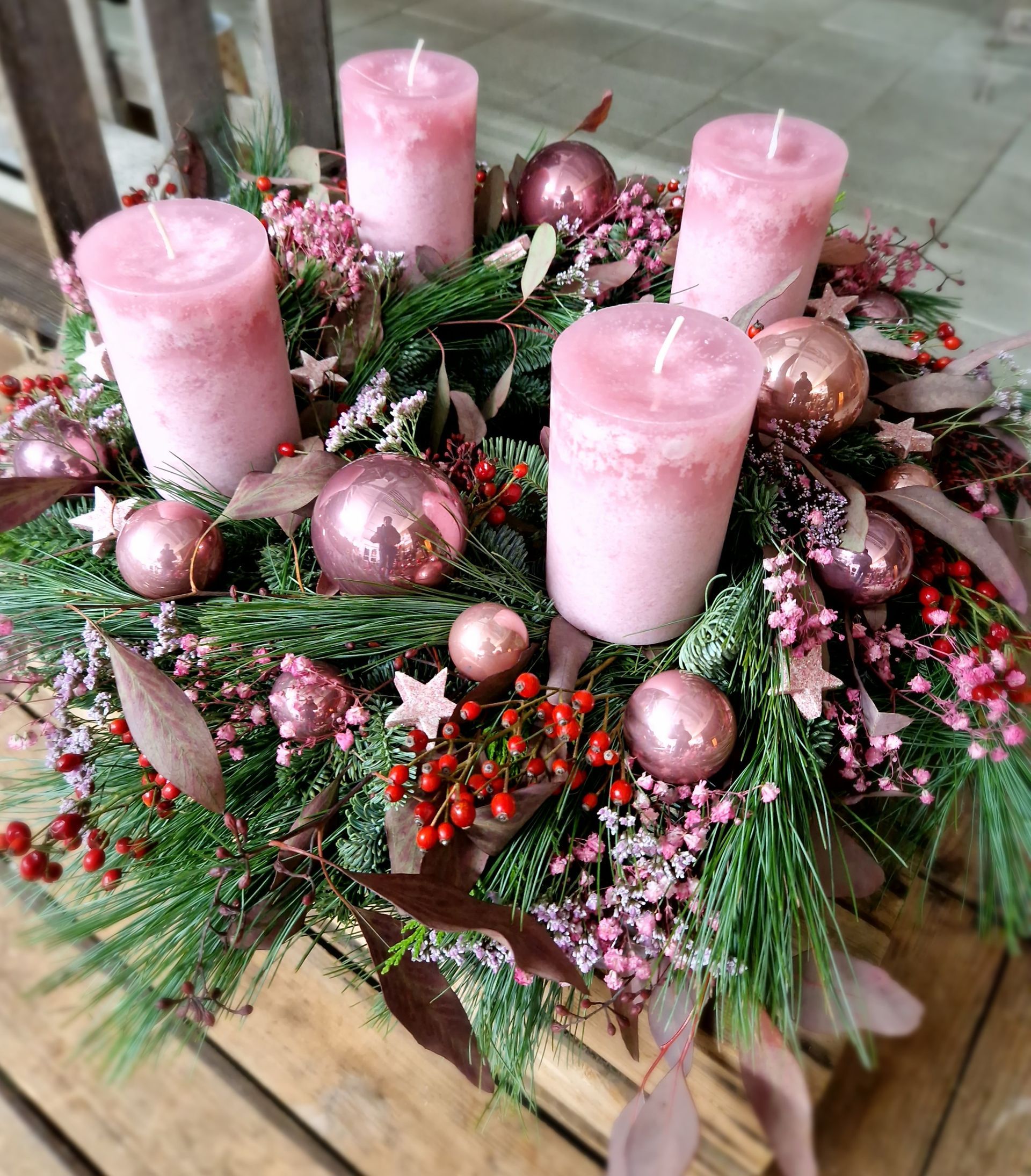 Ein Weihnachtskranz mit rosa Kerzen und Blumen auf einem Holztisch