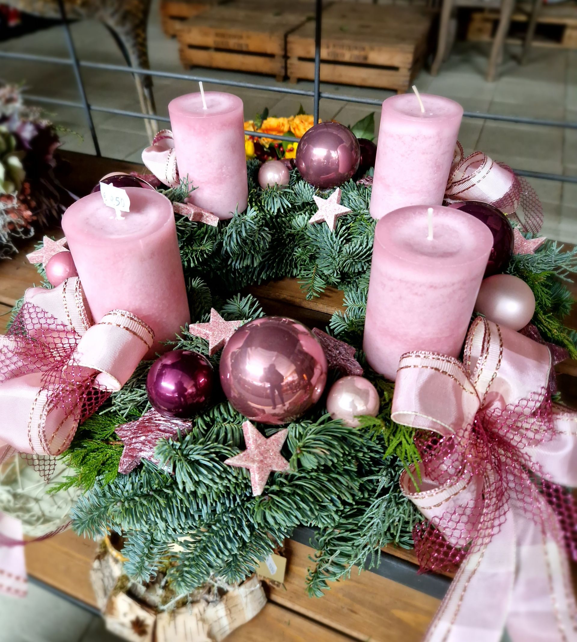 Ein Weihnachtskranz mit rosa Kerzen und Dekorationen auf einem Holztisch.