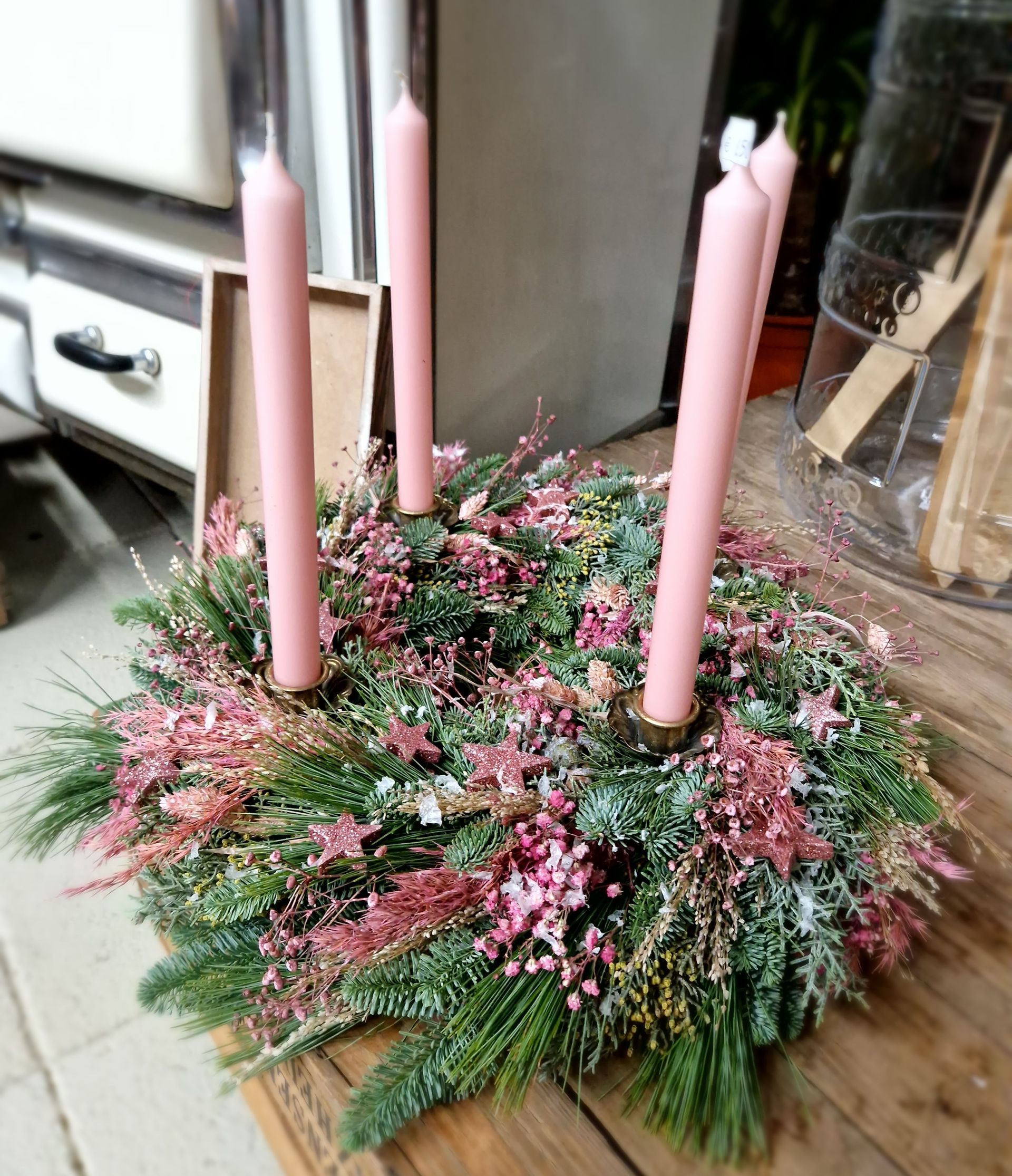Ein Kranz mit rosa Kerzen und rosa Blumen auf einem Holztisch.