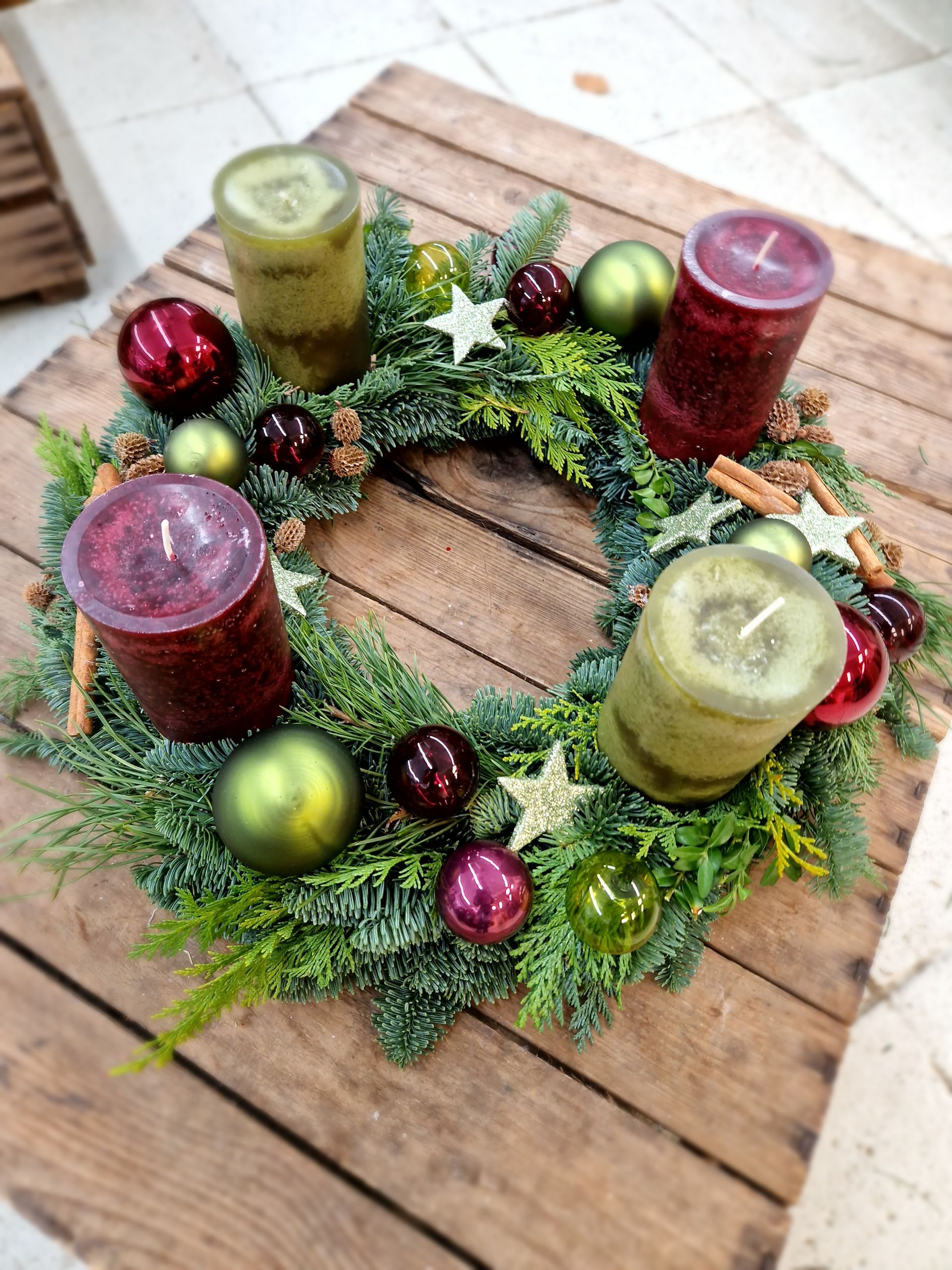 Ein Weihnachtskranz mit Kerzen und Dekorationen auf einem Holztisch.