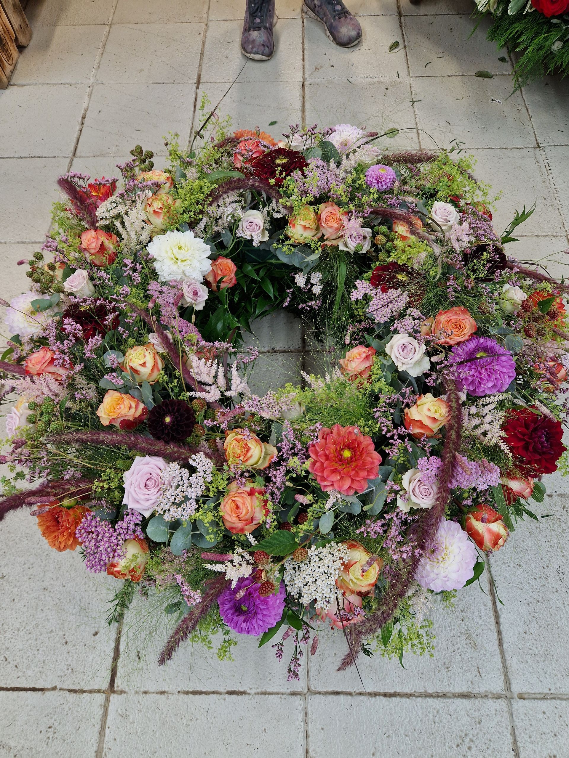 Eine Person steht neben einem Blumenkranz auf einem gefliesten Boden.