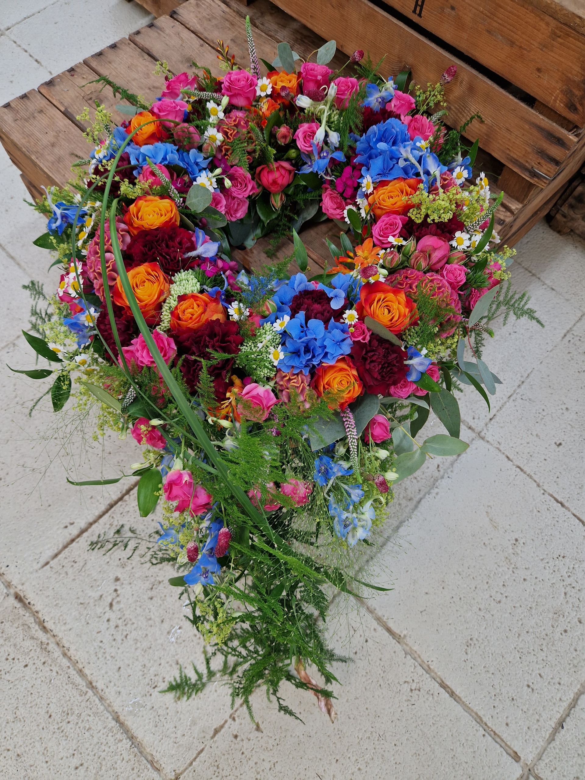 Auf einer Holzpalette liegt ein Kranz aus bunten Blumen.