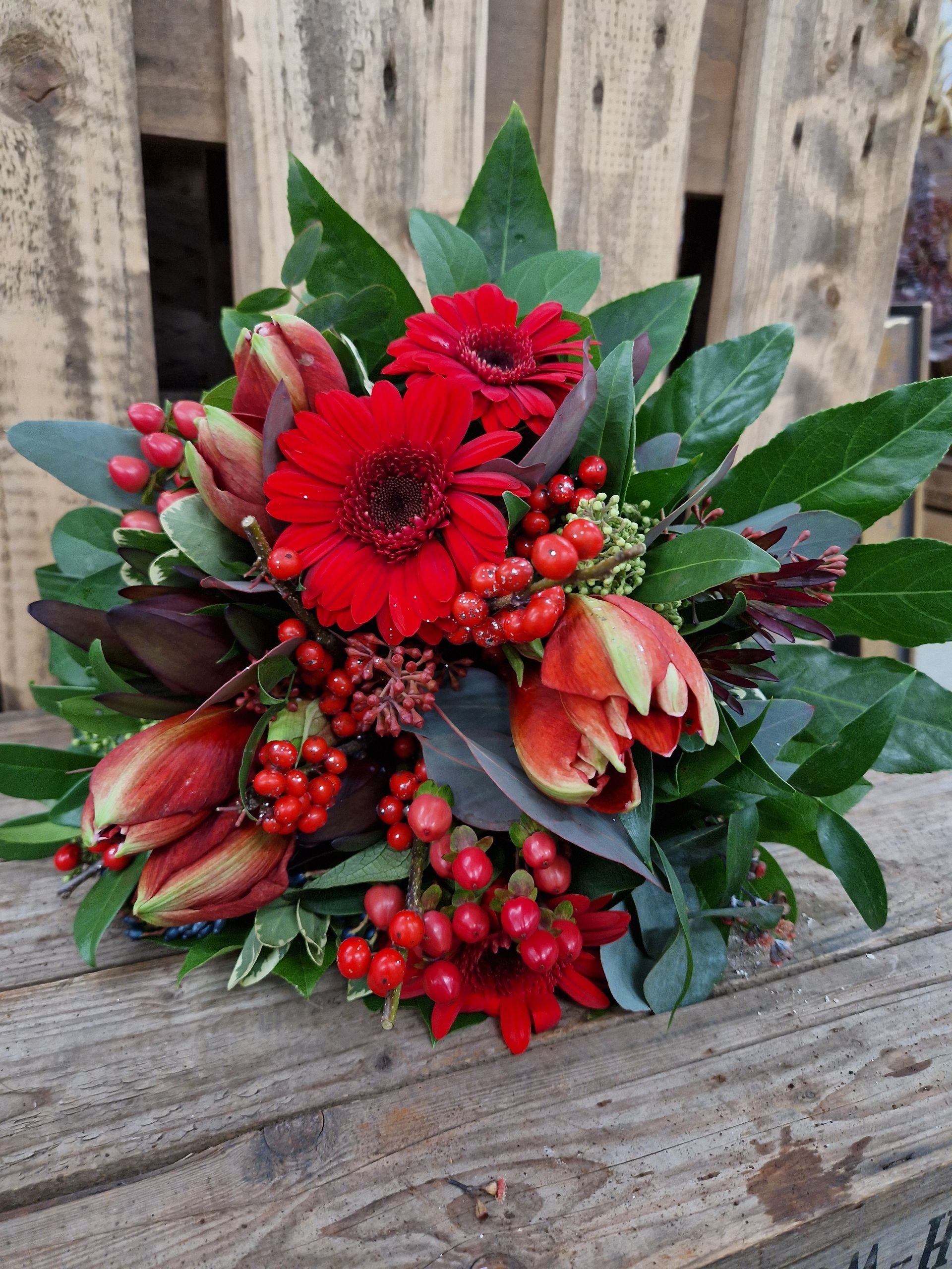 Ein Strauß roter Blumen und Beeren steht auf einem Holztisch.