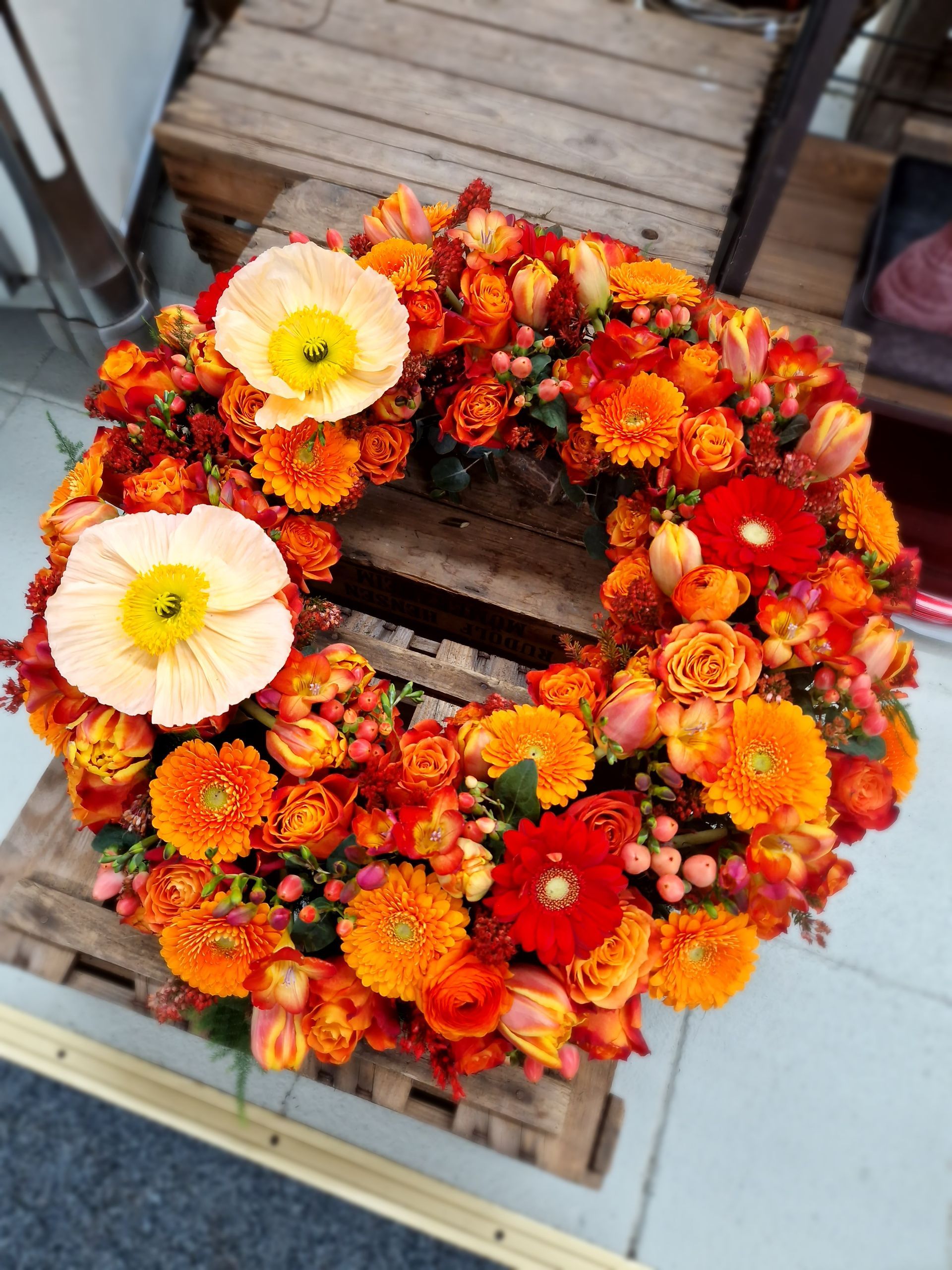 Ein Kranz aus orangen Blumen sitzt auf einer Holzkiste