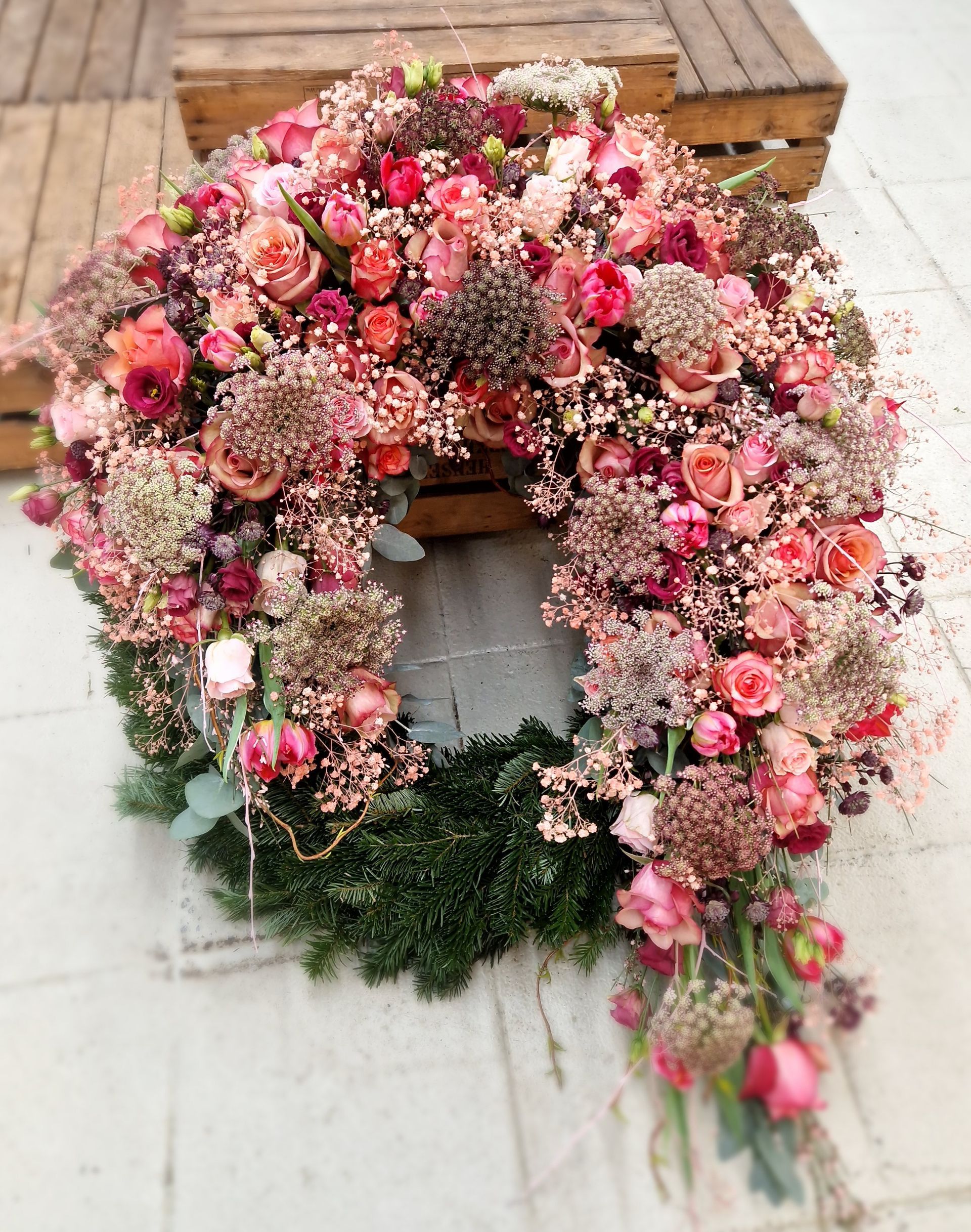 Auf einem Holztisch steht ein Kranz aus rosa Blumen.
