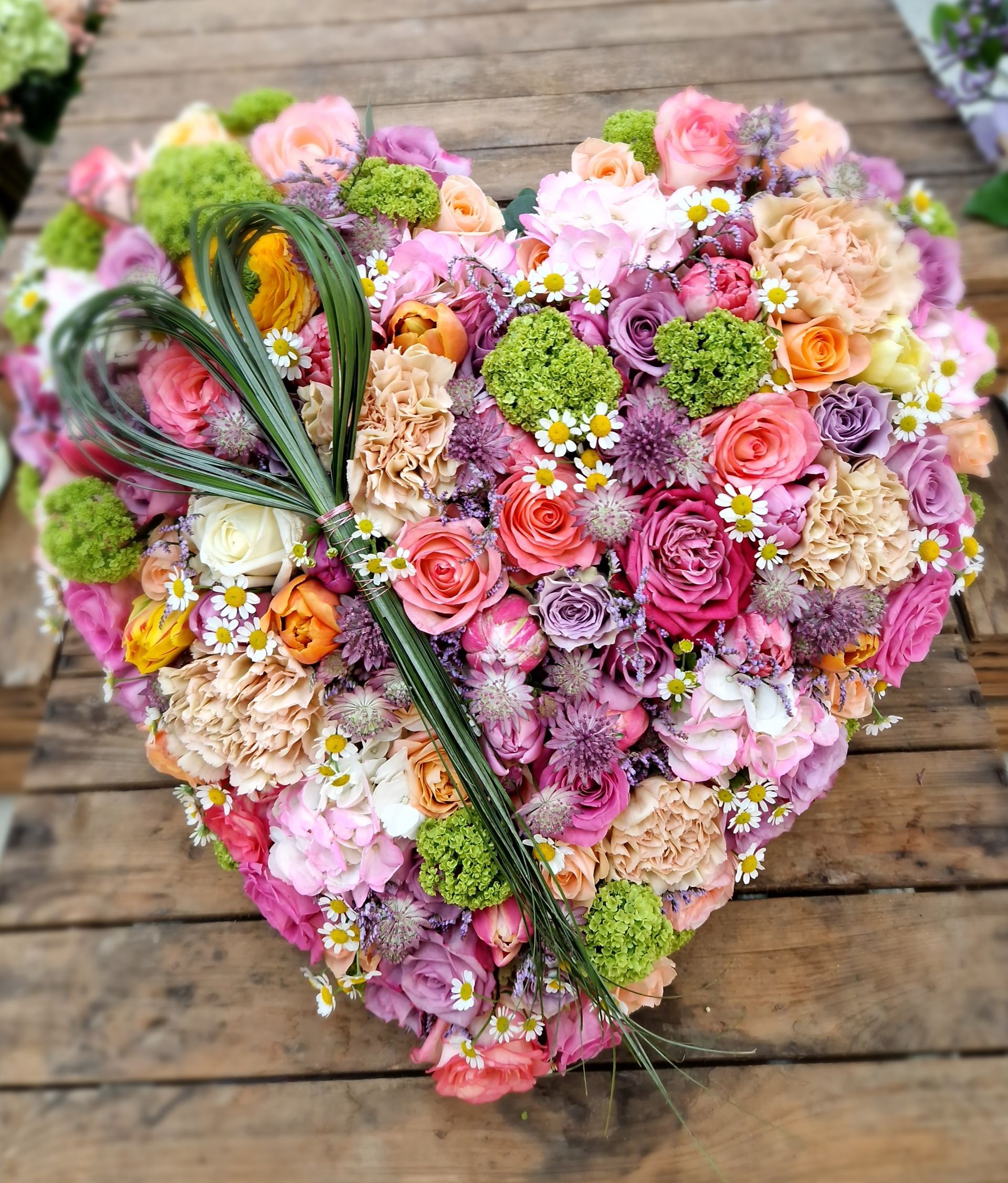 Ein herzförmiger Blumenstrauß steht auf einem Holztisch.