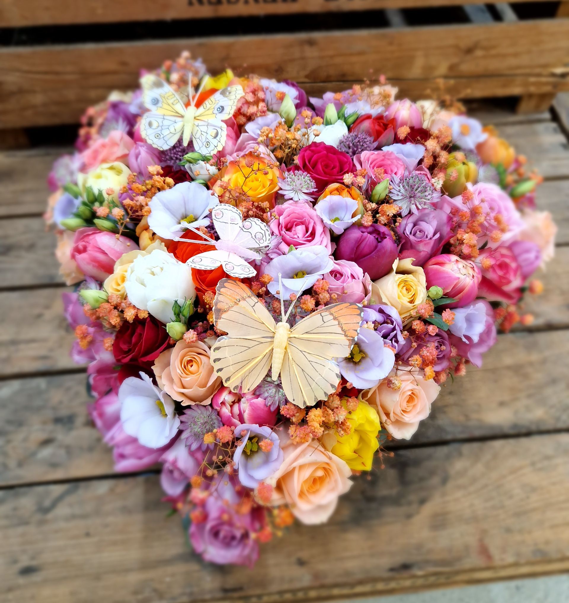 Ein herzförmiger Blumenstrauß mit Schmetterlingen oben drauf