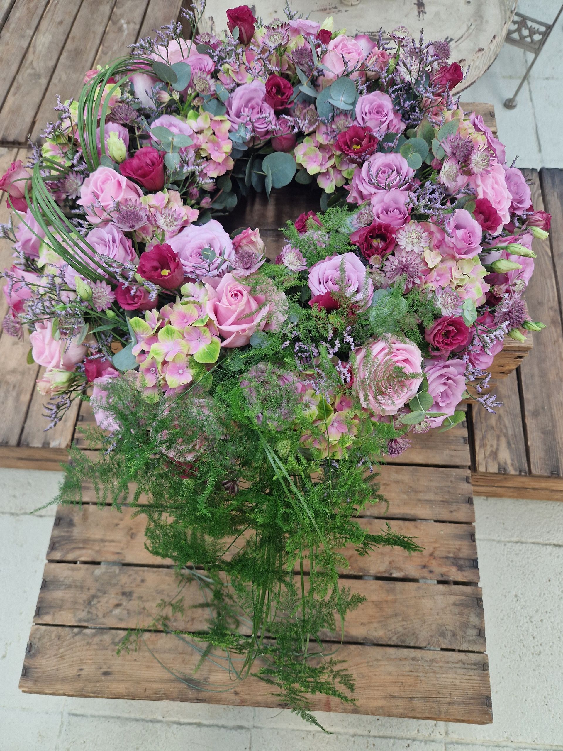 Auf einem Holztisch steht ein Kranz aus rosa Blumen.